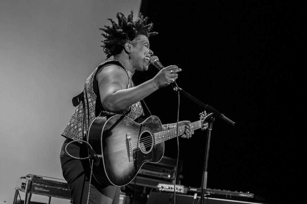 Silhouetted performer passionately plays acoustic guitar while singing on stage in black and white.