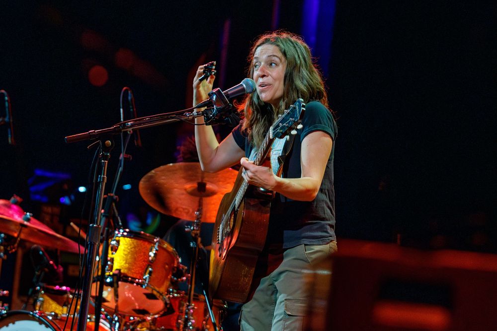 Stage performance with acoustic guitar and drum kit visible in dramatic concert lighting.