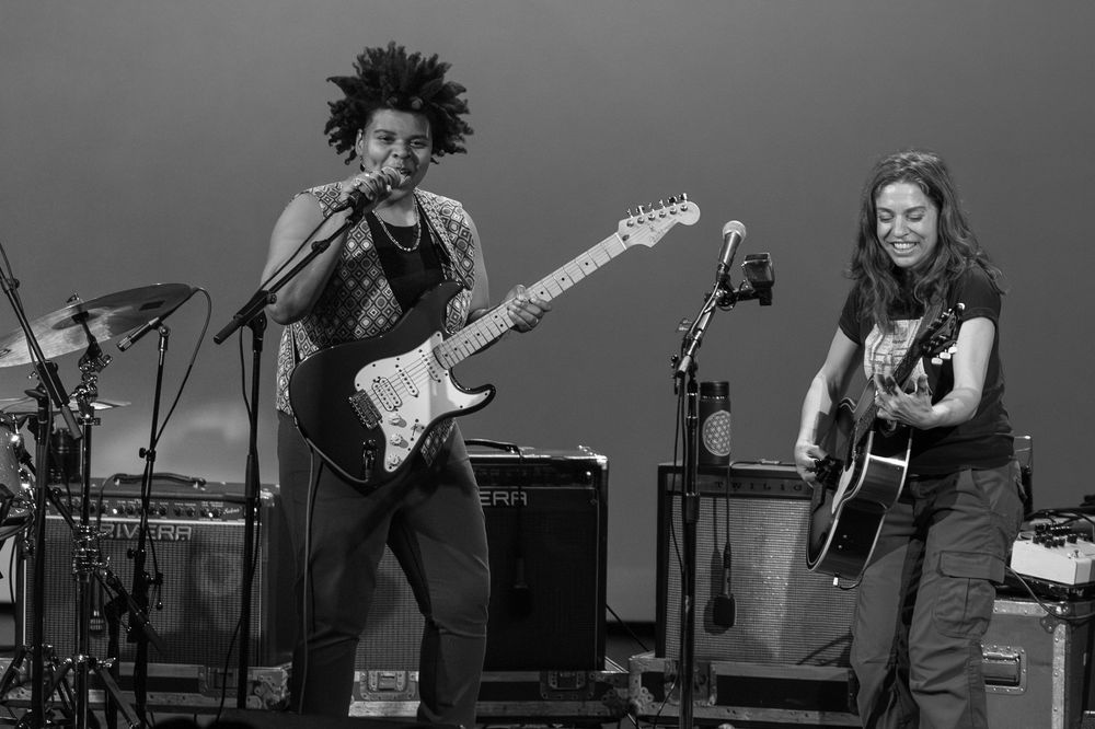 Black and white photo of two musicians performing on stage with electric and acoustic guitars.