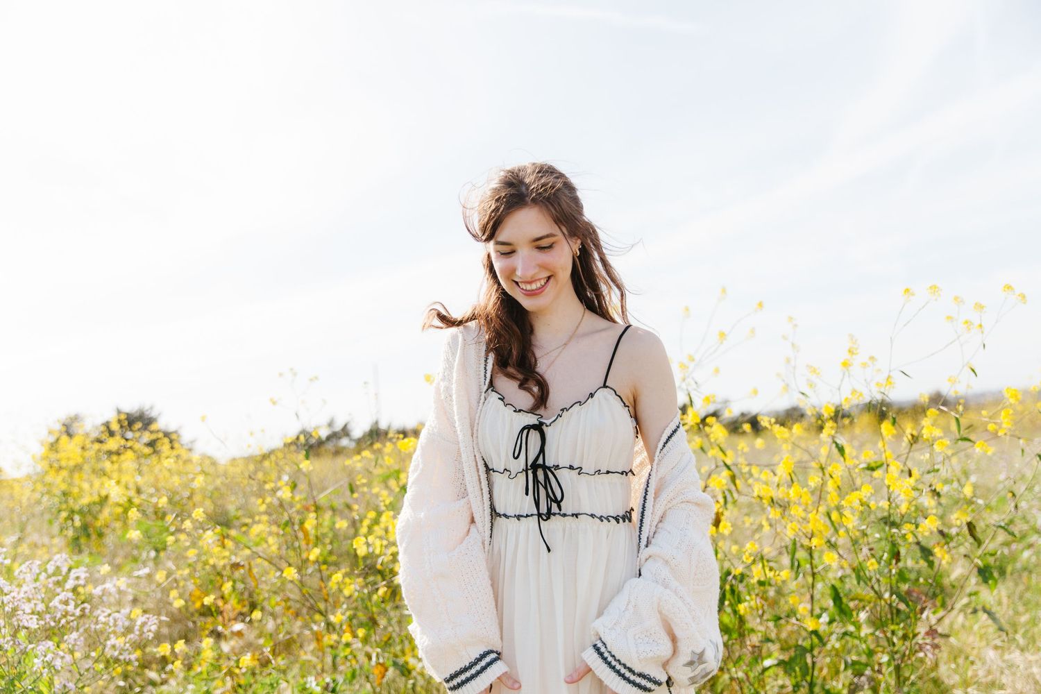 woman smiling looking down in all cream colored clothing in a wildflower field