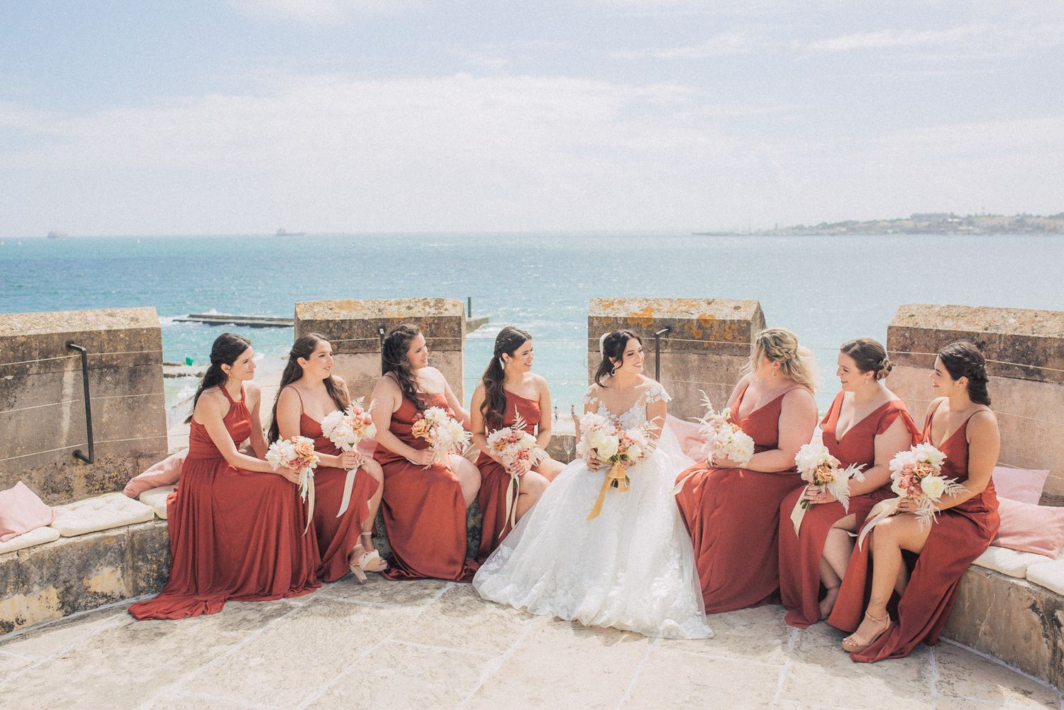 Wedding party holding luxurious white and blush bouquets at forte da Cruz. captured by a Lisbon destination wedding photographer