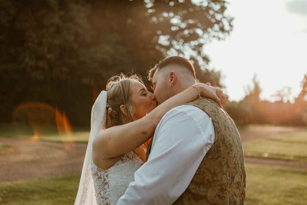 A romantic sunset wedding moment with two figures embracing outdoors in warm golden light.