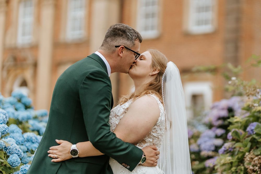 A romantic moment captured between two people among blooming hydrangea flowers at a brick facade estate.