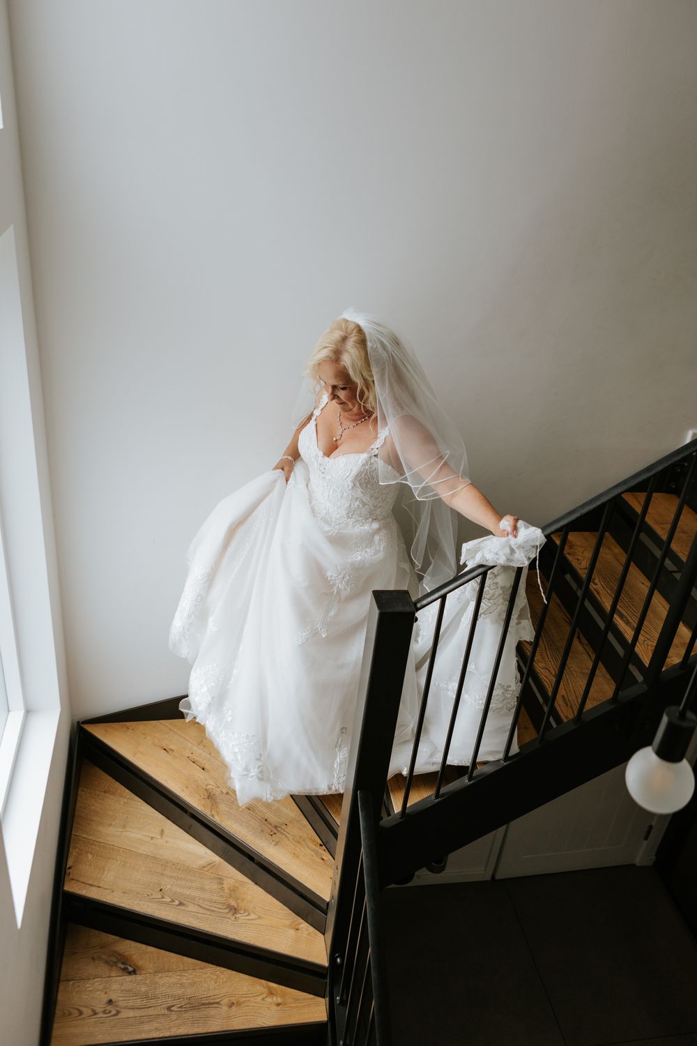 A bride in a flowing white wedding dress ascends a wooden staircase with black metal railings in a sequence of photos.