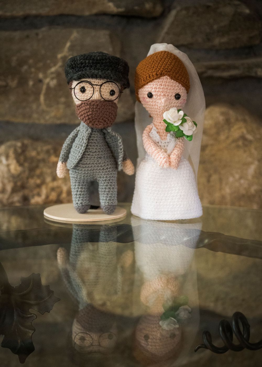 Handmade crochet wedding couple dolls with glasses and flowers against stone background.