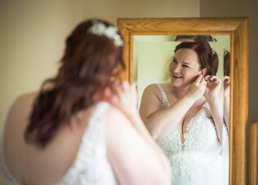 A reflection shows a person putting on jewelry while getting ready in front of a wooden framed mirror.