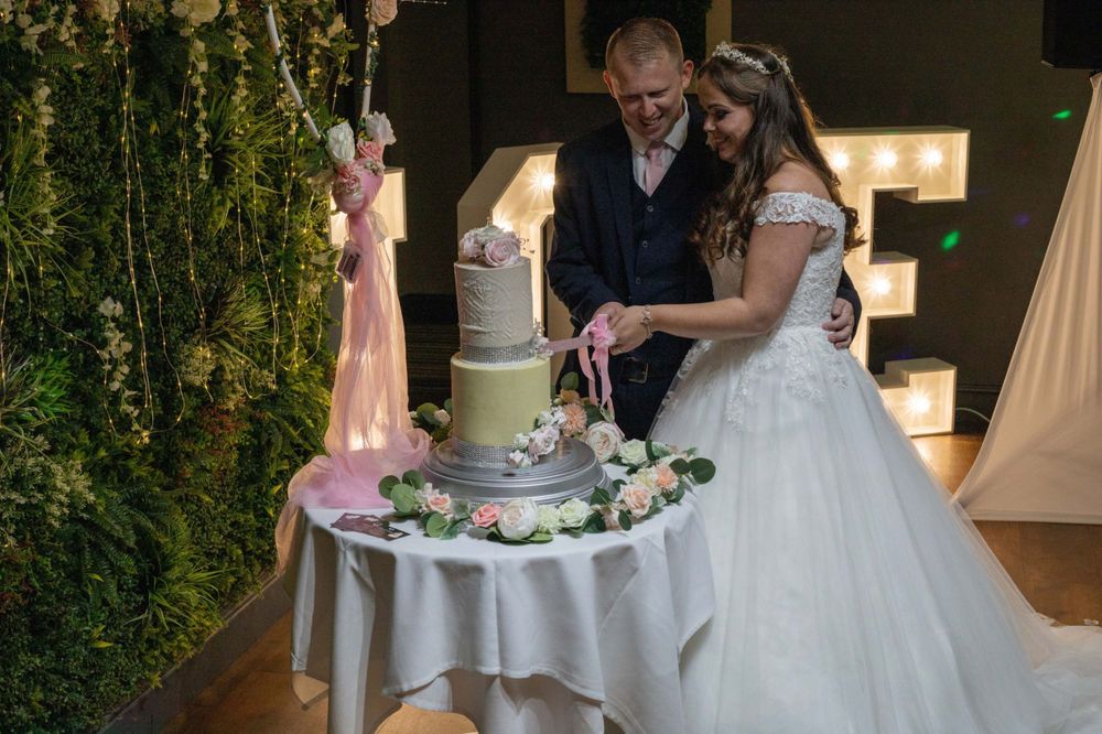 A couple in wedding attire cutting their white and gold tiered wedding cake at their reception.