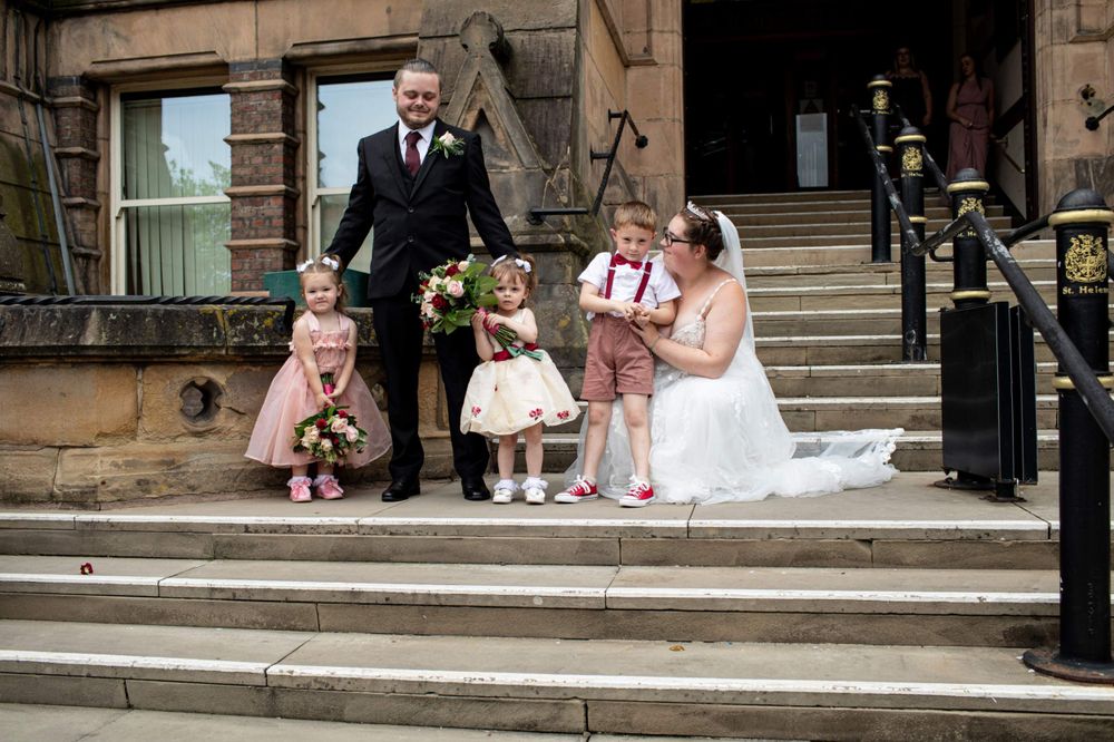 Wedding party sits together on grand stone steps outside a historic building during photo session.