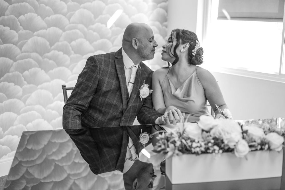 A romantic black and white wedding photo of a couple sharing an intimate moment at their reception table.