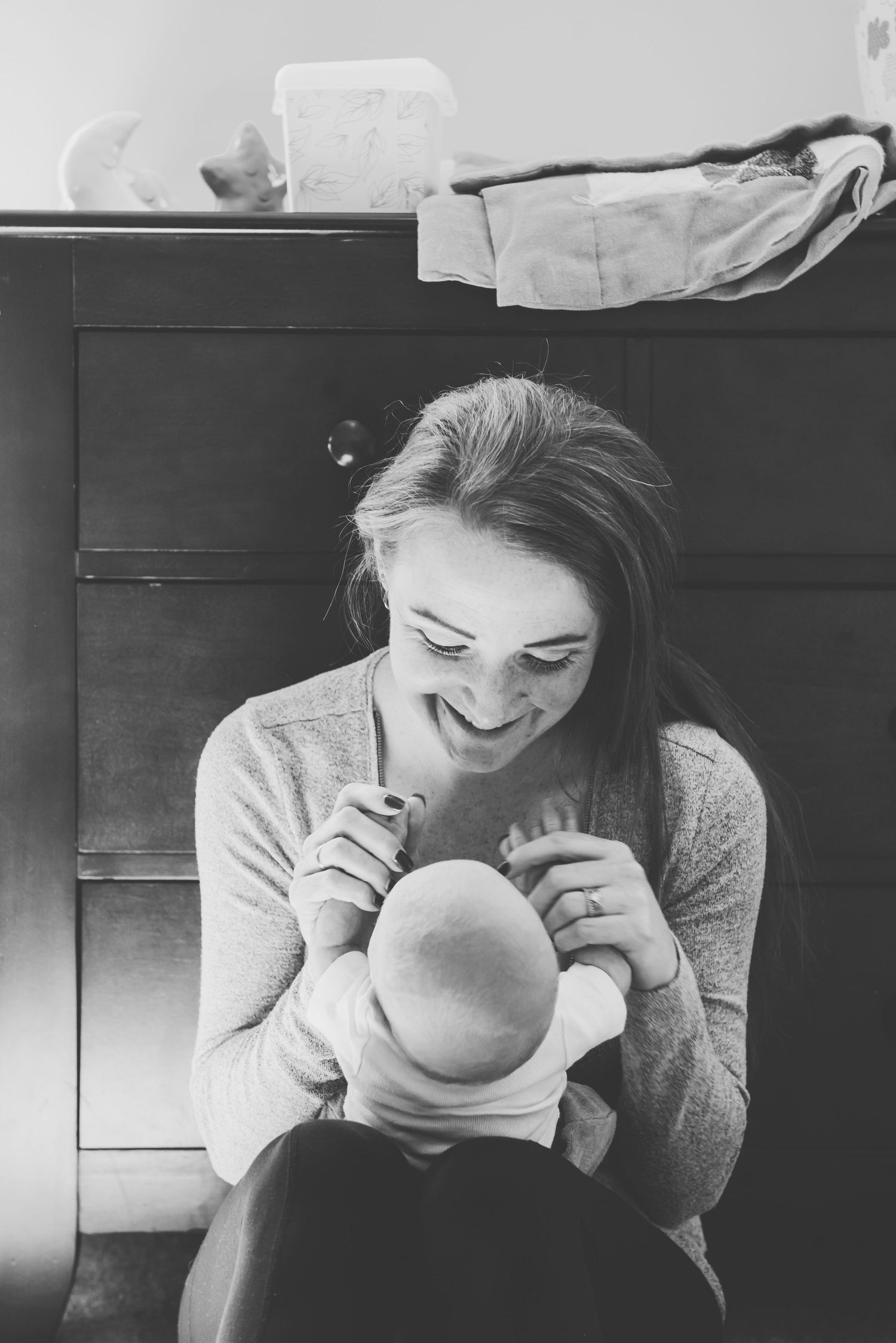 A candid black and white photo showing a tender \moment as a baby is being held and adored by his mother.