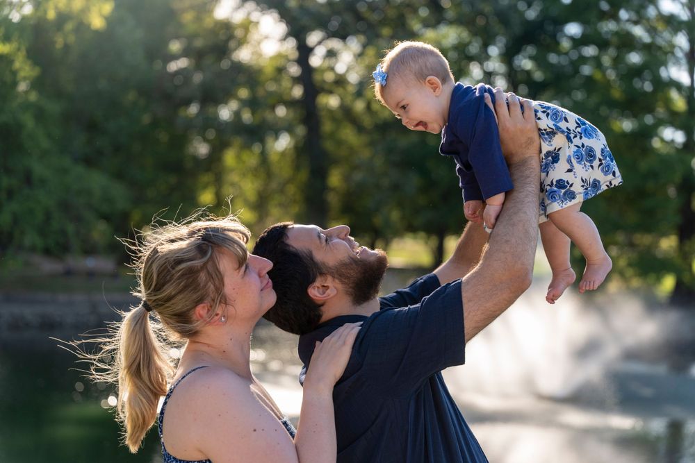 Parents lift and play with their joyful baby outdoors during a sunset photoshoot.