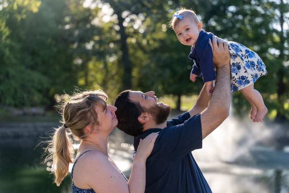 A couple lifts their laughing baby high in the air during an outdoor photo session.