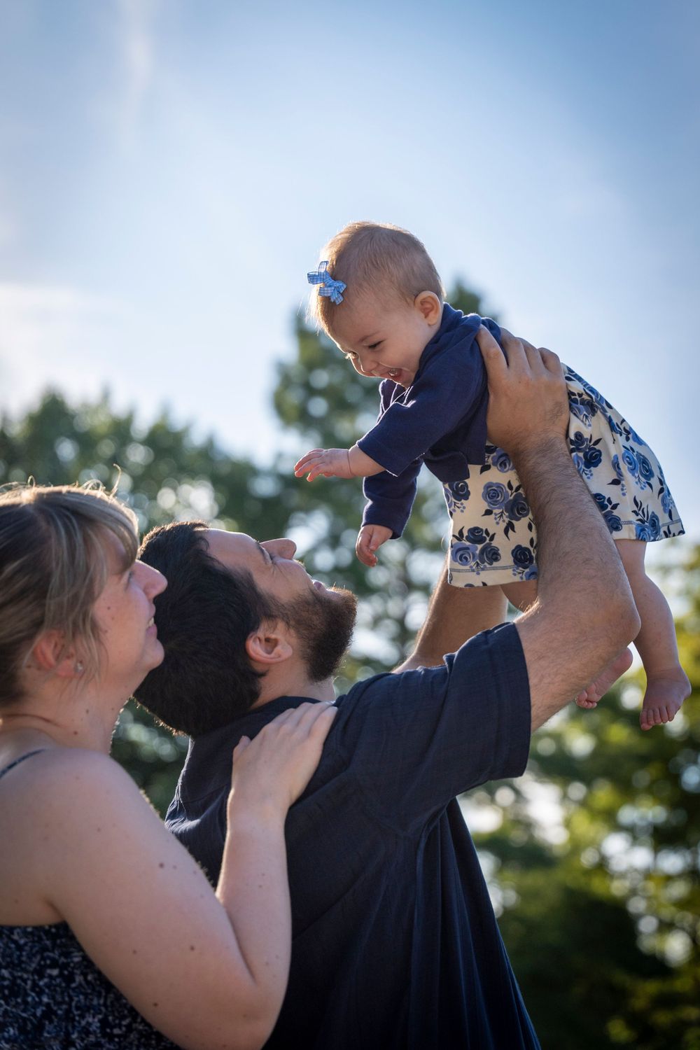 Joyful family moment as a baby in a blue and white outfit is lifted high into the sunny sky.