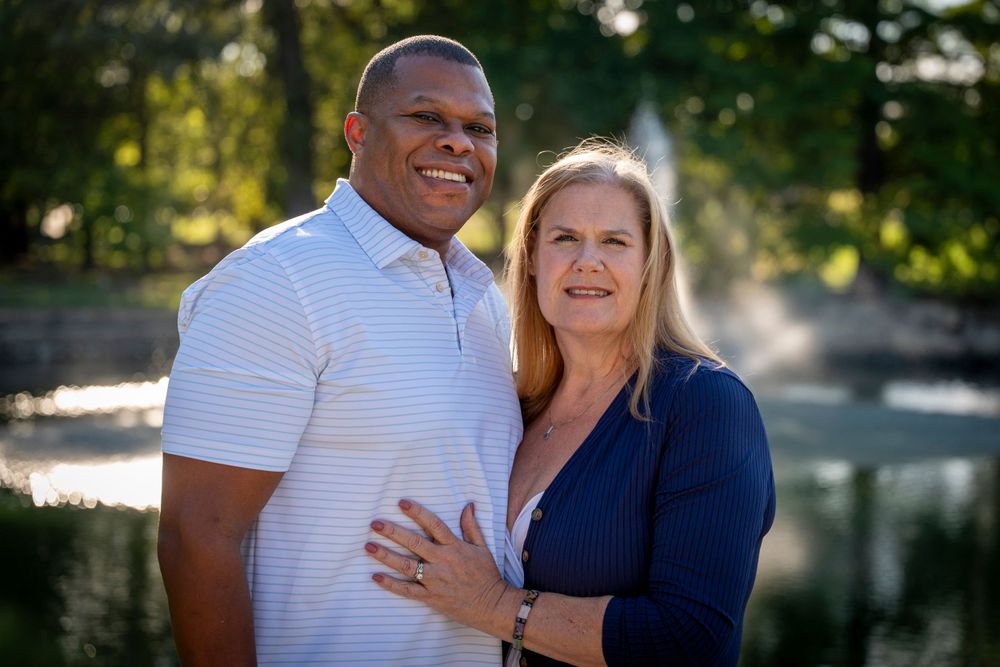 Couple poses for a romantic portrait by a scenic pond on a sunny afternoon.