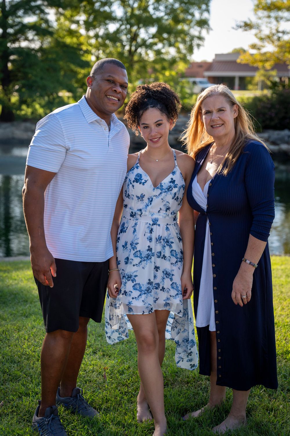Three people pose casually together by a pond during golden hour.