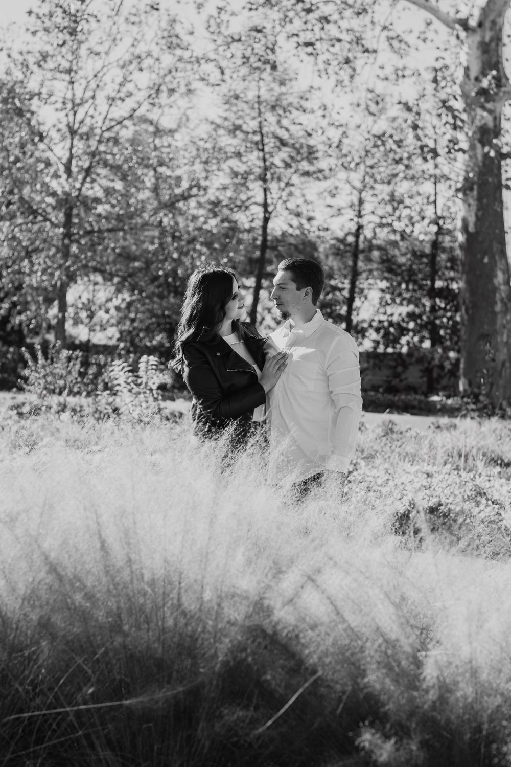 Black and white photo of couple standing together in a misty field with trees.