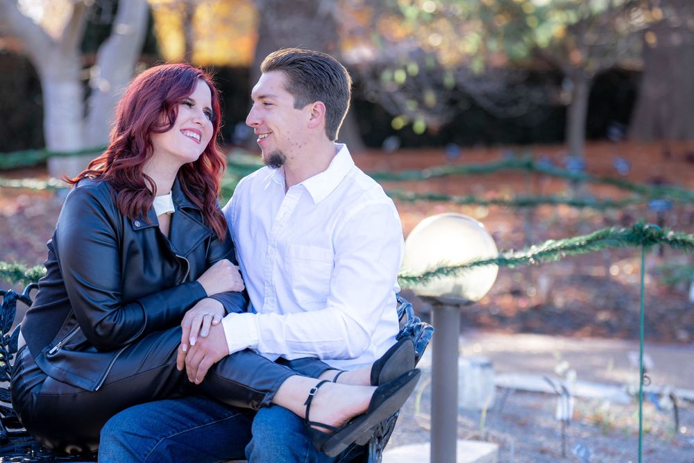 A couple shares a tender moment while sitting on a bench in a fall garden setting.