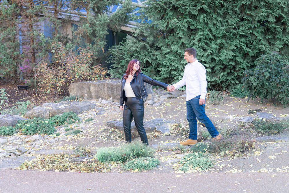 A couple holding hands while walking through a rustic outdoor setting.