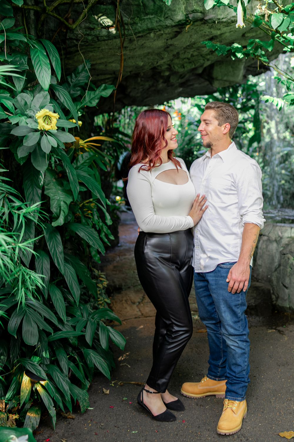 A couple shares an intimate moment in a garden pathway surrounded by exotic plants and flowers.