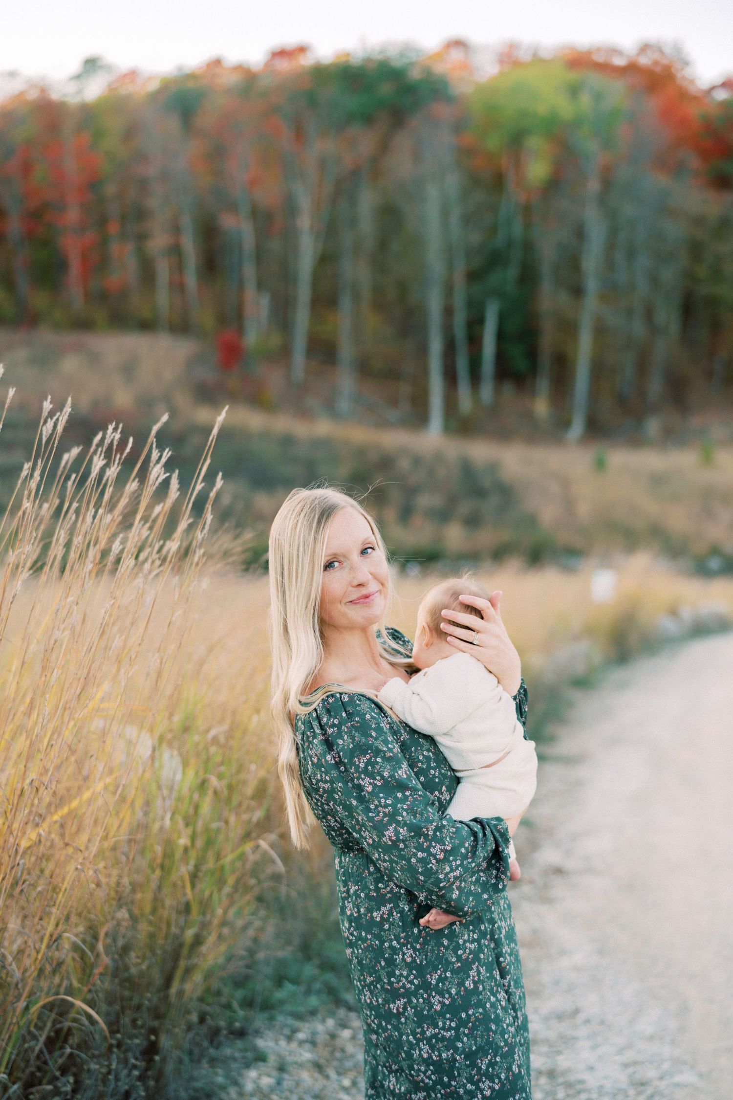 Mother and baby sharing a tender moment against autumn trees and tall grass.