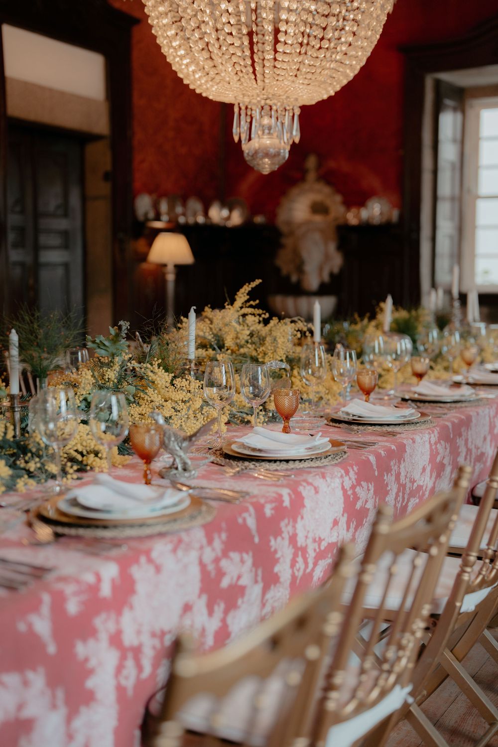 An elegant wedding table setting with a crystal chandelier, pink tablecloth, and delicate floral arrangements.