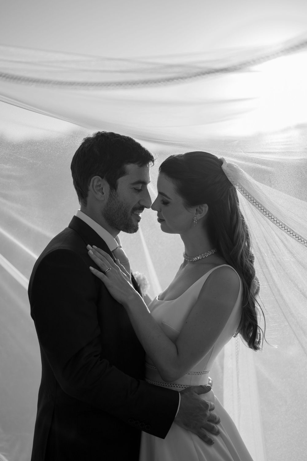 Romantic black and white portrait of newlyweds embracing under flowing veil.