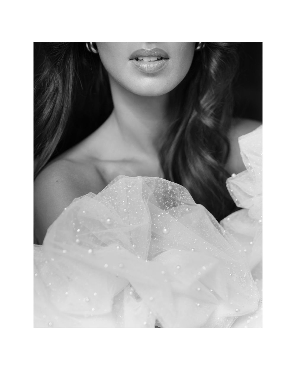 A person wearing a white wedding dress with a ruffled neckline and sleeves in a black and white artistic portrait.