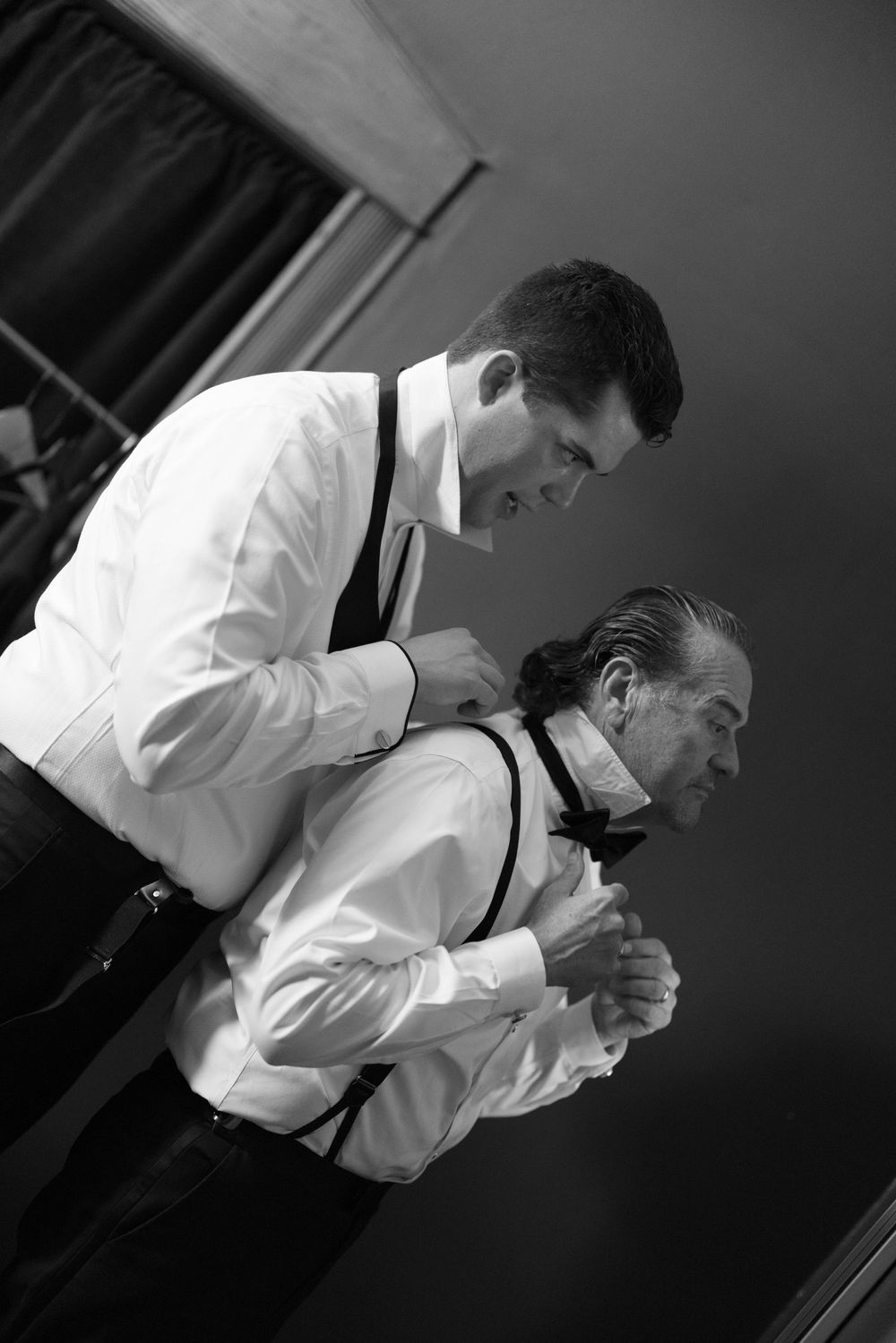 Two performers in white dress shirts and suspenders stand together in a dramatic black and white stage performance.