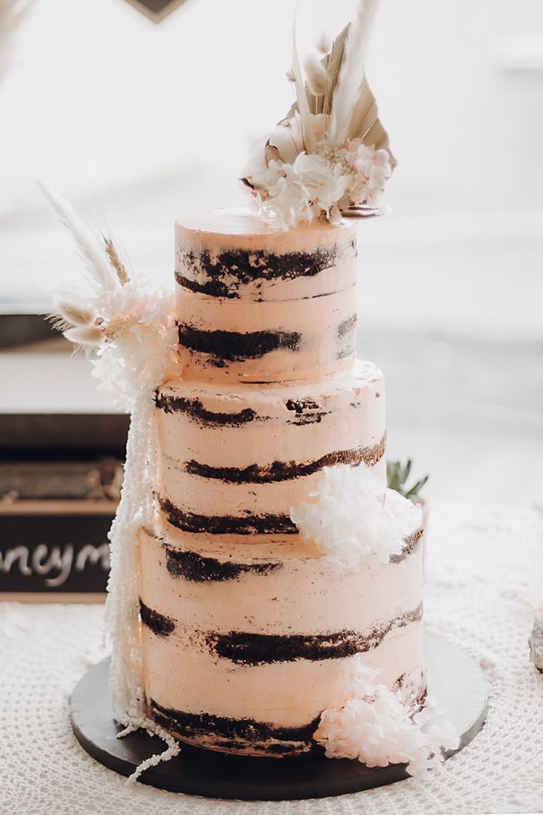 A rustic semi-naked wedding cake with three tiers decorated with dried pampas grass and delicate floral accents.