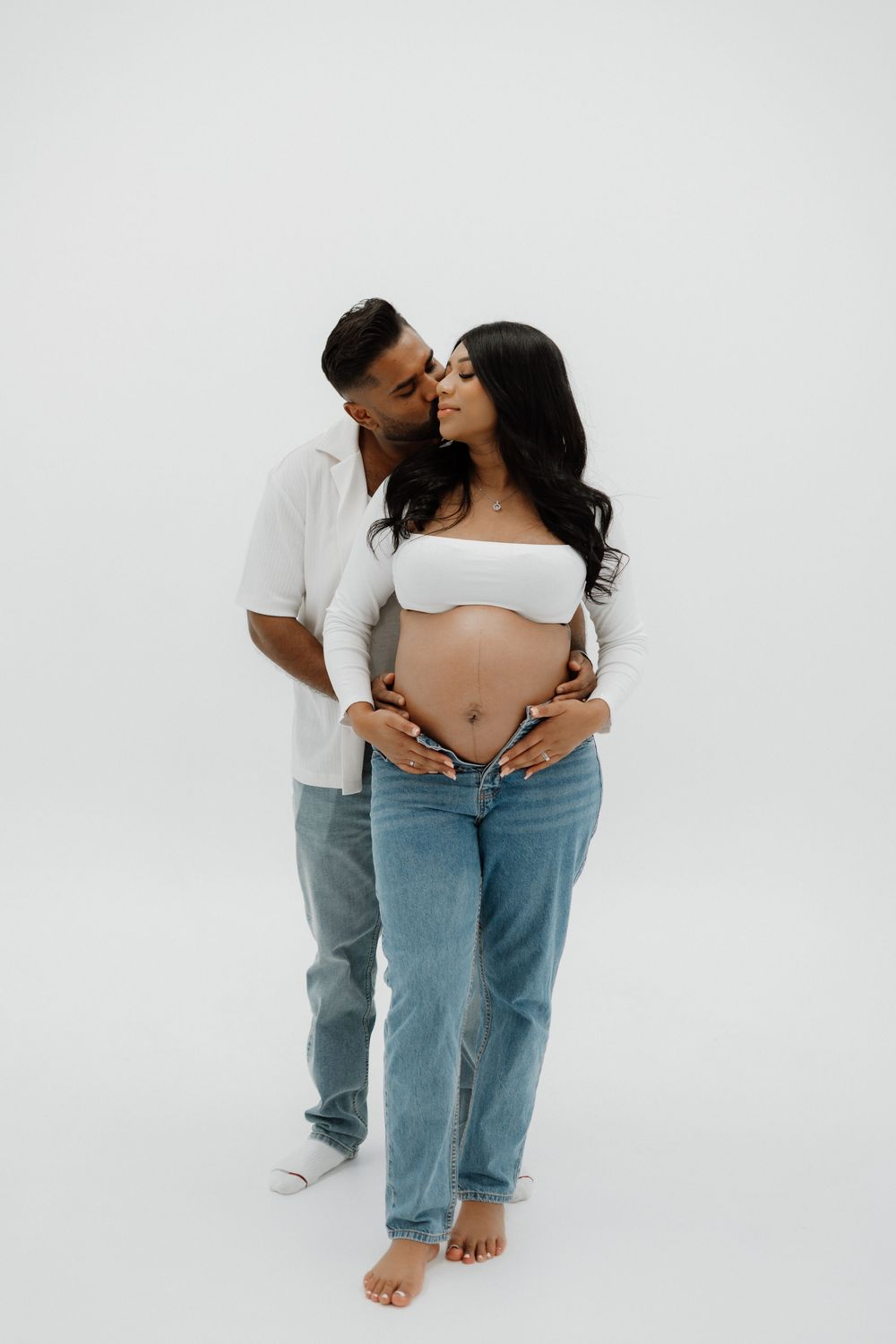 A couple in casual attire embraces lovingly on a white backdrop in a series of artistic romantic poses.