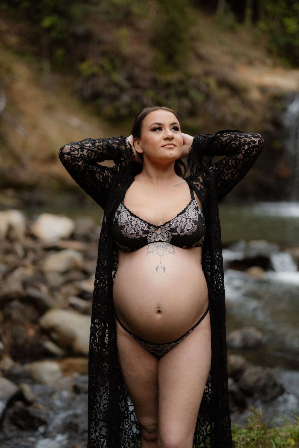 Maternity photo shoot near a stream with a pregnant person wearing black lace and lingerie in nature.