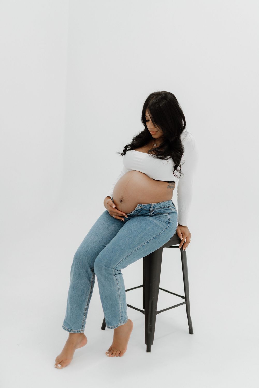 Artistic sequence of someone wearing blue jeans seated on dark metal stool against white backdrop in various poses.
