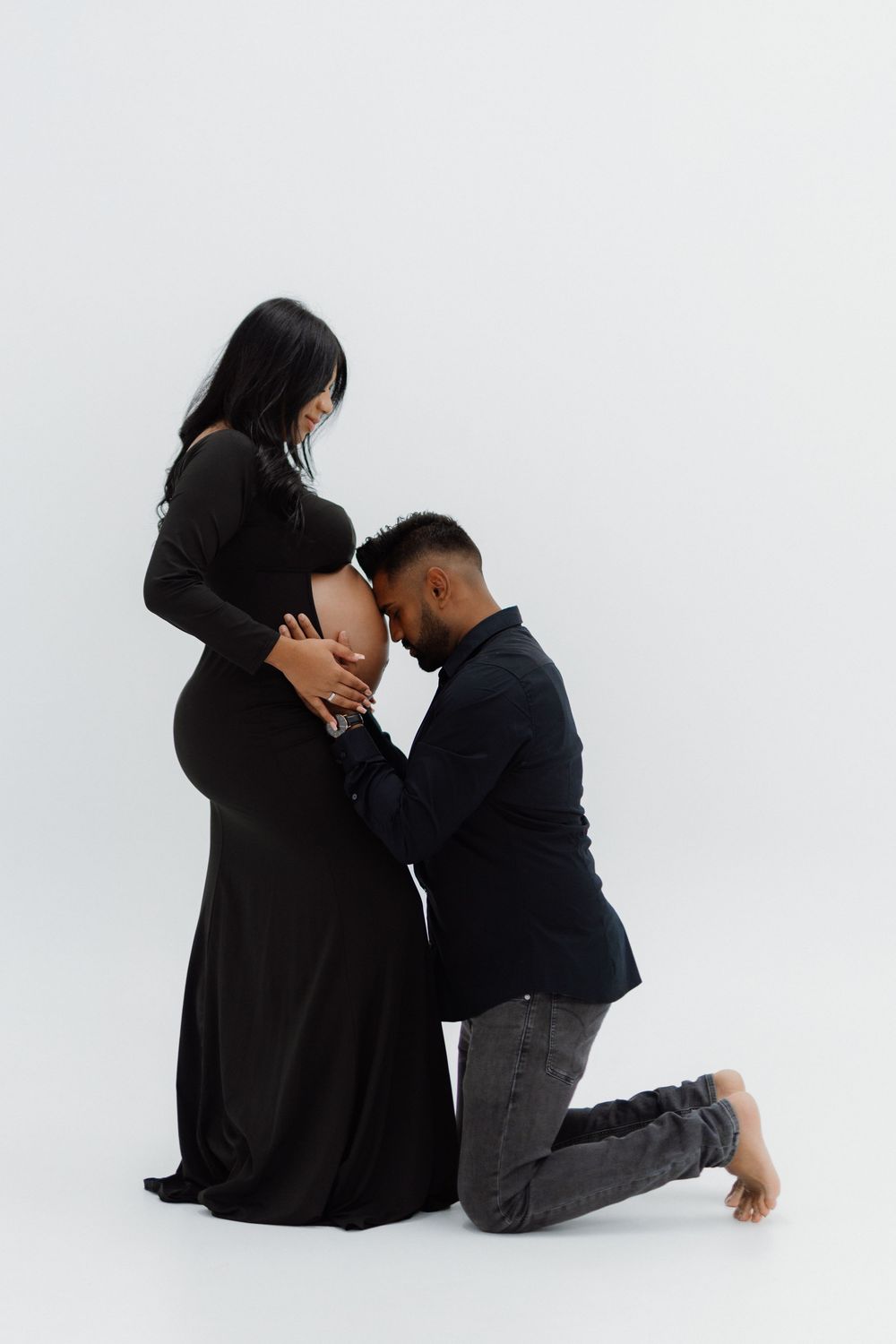 A tender maternity moment captured against white backdrop with couple in black and grey attire.
