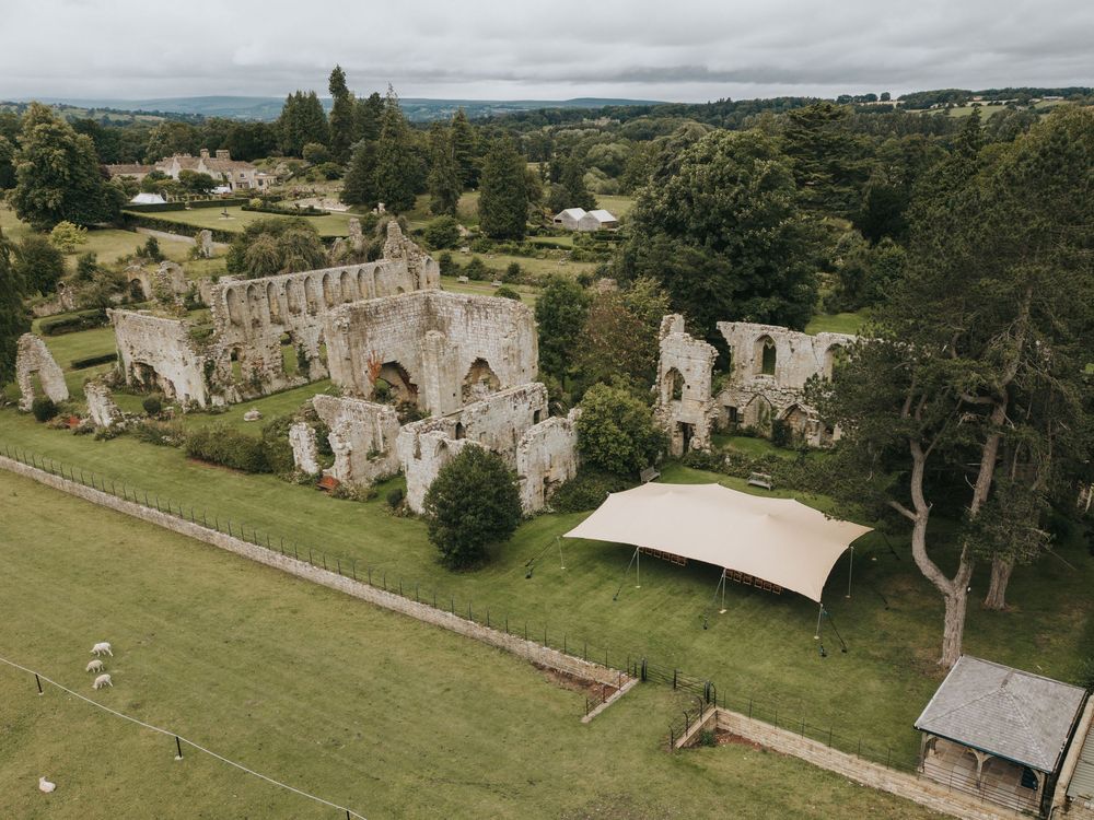 Aerial view of a historic stone abbey ruins surrounded by green countryside and gardens.