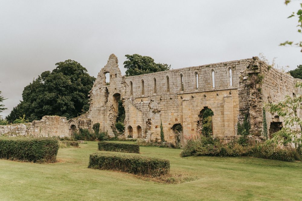 Ancient stone abbey ruins with arched windows and well-maintained green lawn in the foreground.