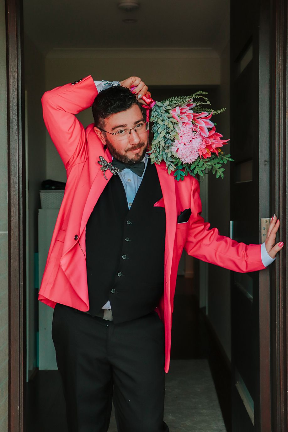 Wedding party member in black vest and coral jacket posing playfully in a hallway sequence.