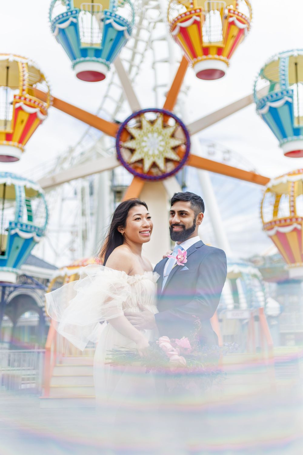 Wedding couple sharing joyful moments at a colorful carnival with festive rides in the background.