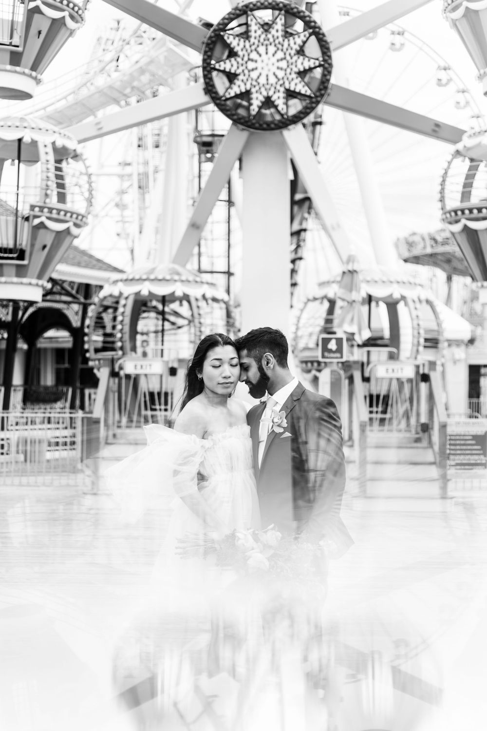 Couple in wedding attire embracing under ornate carousel lighting fixtures.