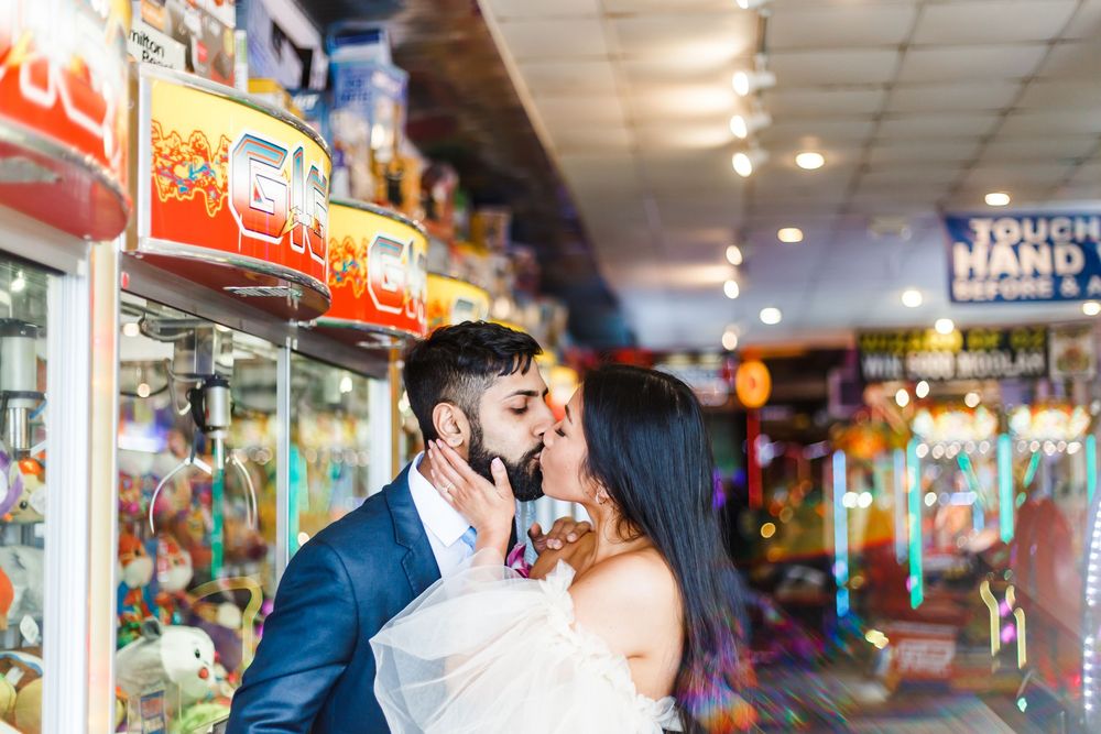 A couple shares an intimate moment in an arcade with colorful game machines in the background.