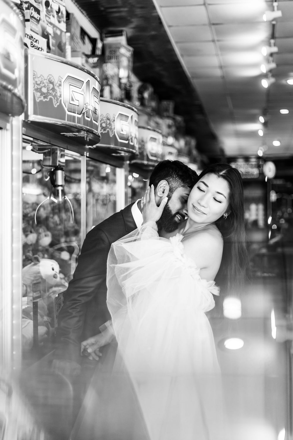 A romantic couple embraces in front of illuminated arcade games in a dimly lit arcade setting.