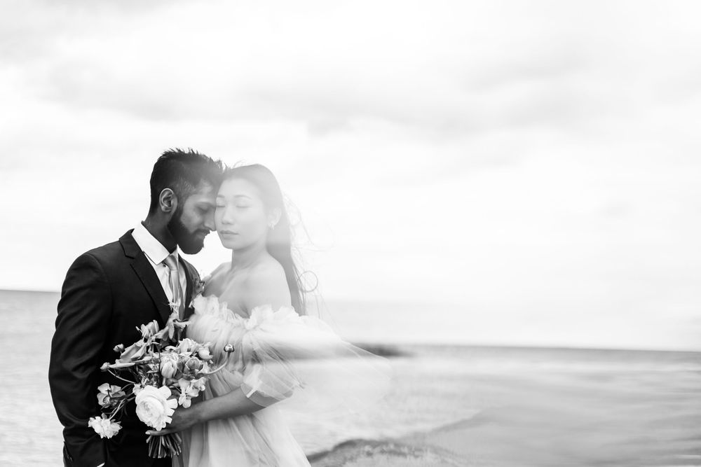 Black and white portrait of couple in wedding attire sharing an intimate moment by the sea.