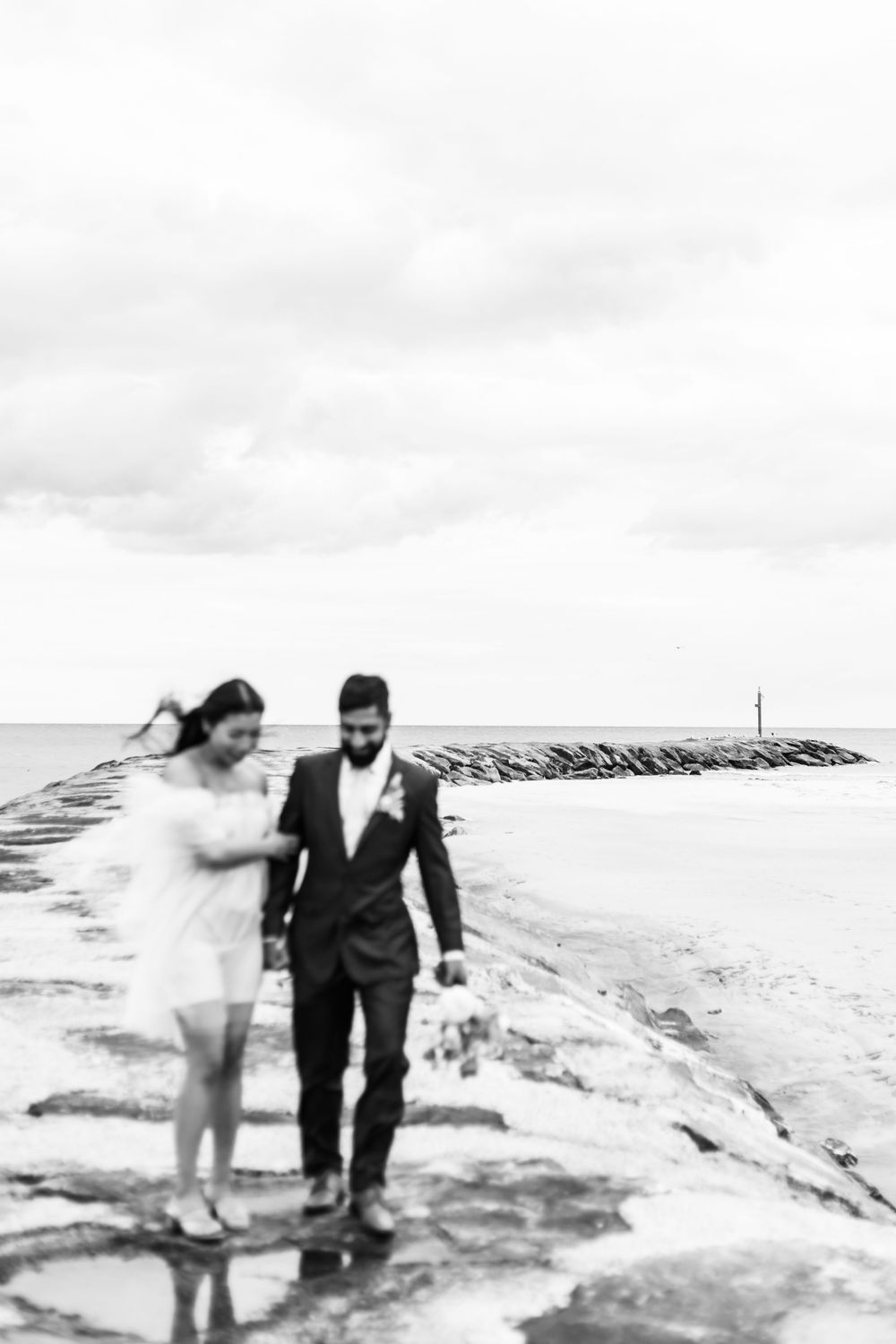 Black and white photo of couple walking together along a rocky oceanside path.