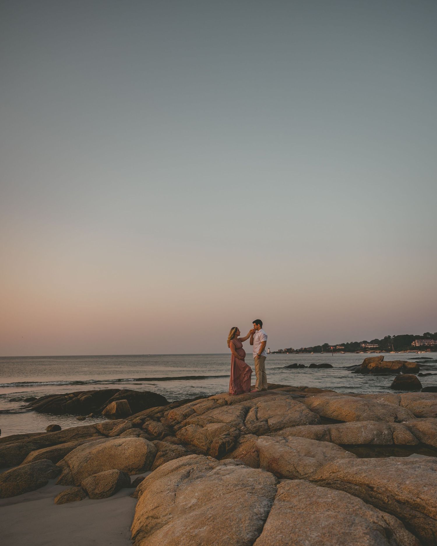 Couple walks along scenic rocky coastline at sunset by the ocean in Ogunquit, Maine.