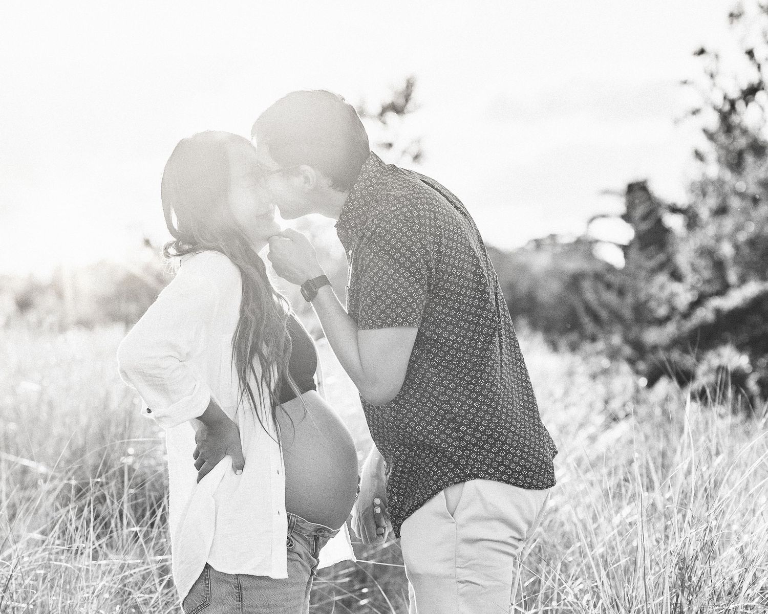 Black and white photo series of a couple sharing intimate moments in a sun-lit grassy meadow.