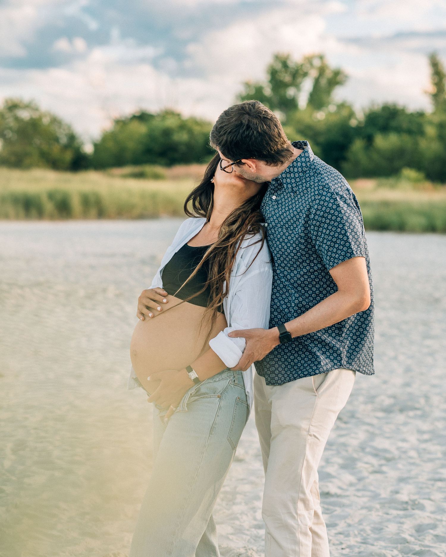 A romantic couple embraces on a sunset beach shore with soft golden light filtering through the scene.