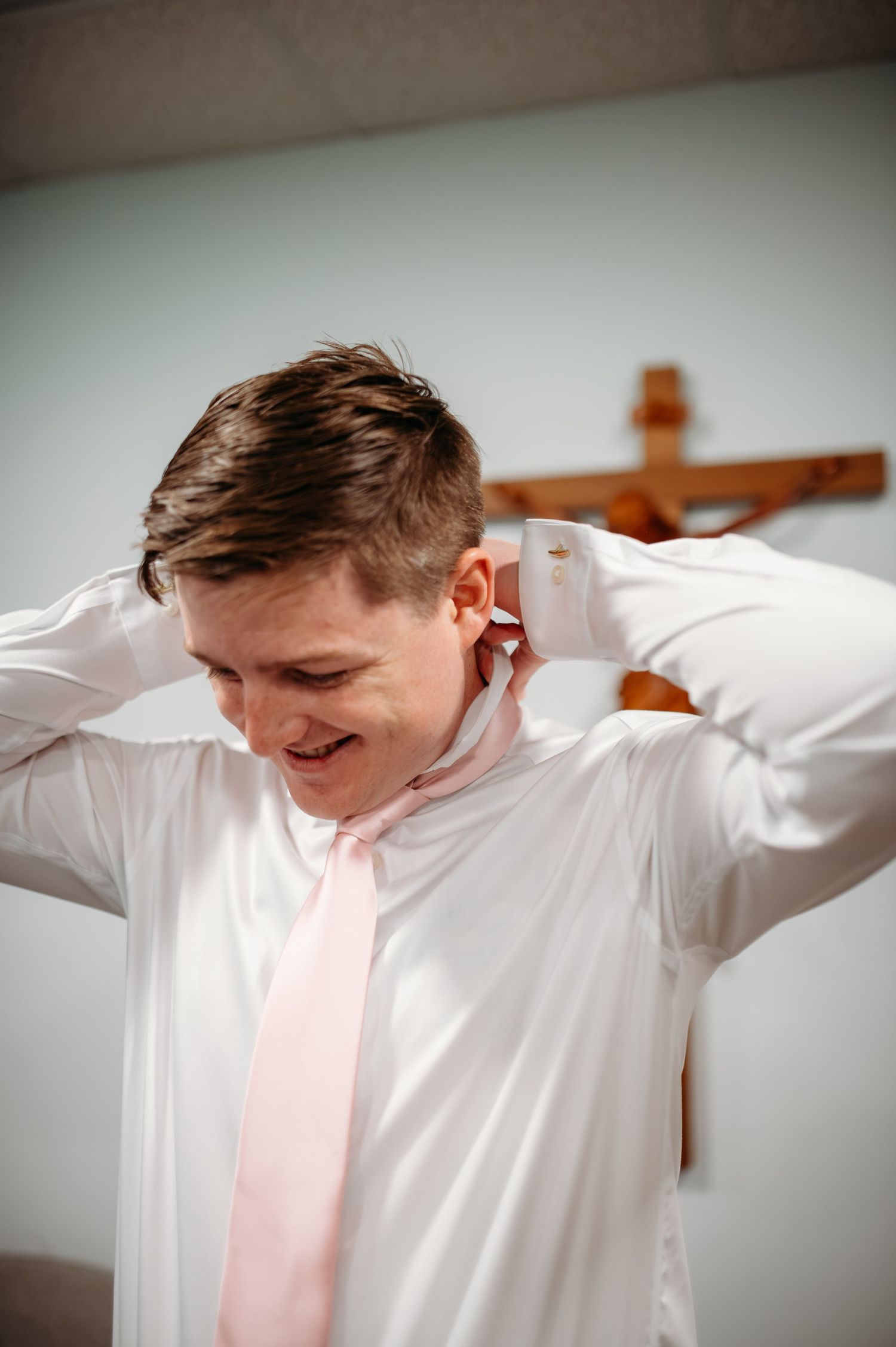A sequence showing someone putting on a white dress shirt and adjusting a light pink tie against a soft, blurred background.
