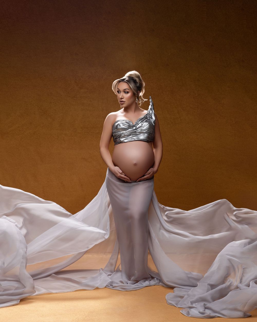 Artistic maternity photo series showing figure in flowing gray fabric against brown backdrop.