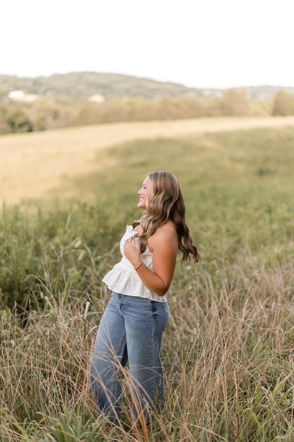 Person in blue jeans laughs joyfully while spinning through a golden meadow at sunset.