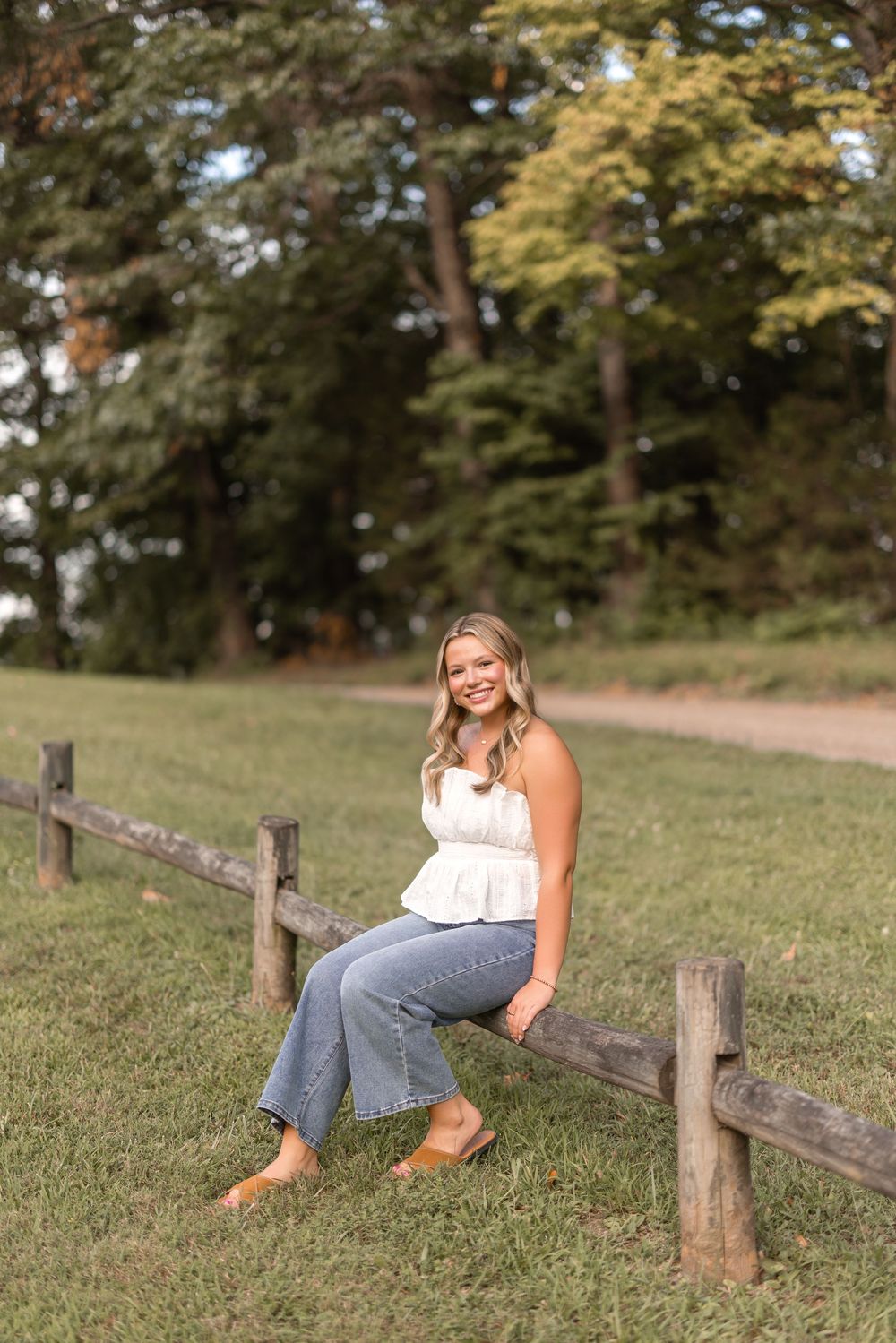 Candid poses in nature as someone leans against rustic wooden fence posts in warm lighting.