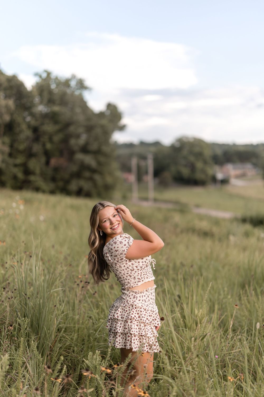 A person in a floral print dress poses carefree in a tall grass meadow on a summer afternoon.